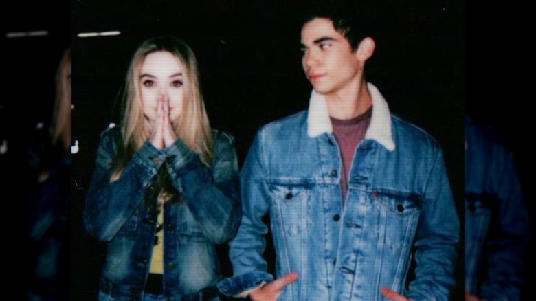 Sabrina Carpenter with her hands in a praying motion over her mouth, with Cameron Boyce standing next to and looking at her