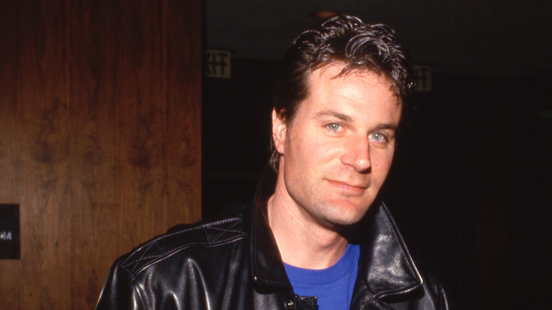 Charles Rocket smiling while wearing a leather jacket and blue shirt