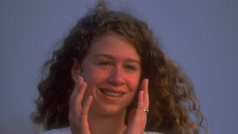 Teenage Chelsea Clinton smiling while holding her hands to face