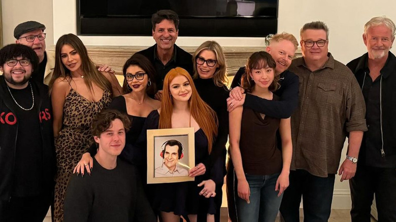 The Modern Family cast posing with a framed photo of Ty Burrell