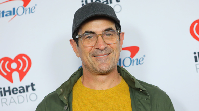Ty Burrell wearing cap and glasses and green jacket on red carpet