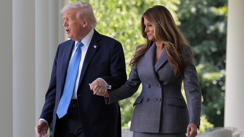 Donald and Melania Trump holding hands awkwardly as they walk towards the White House rose garden.