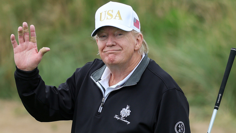 Donald Trump smiling and waving on a golf course