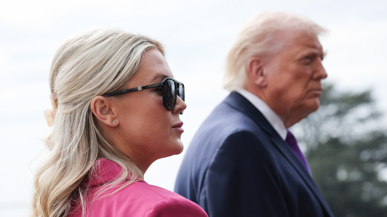 Karoline Leavitt wearing sunglasses and a pink blazer with Donald Trump in the background