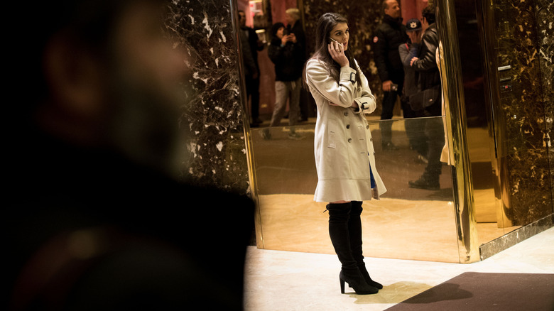 Hope Hicks on phone wearing trench coat and black boots