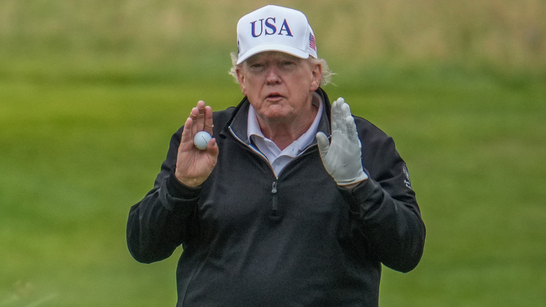 Donald Trump gestures to someone while playing golf.