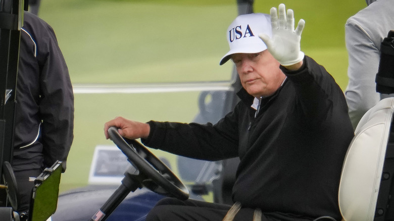 Donald Trump waves to onlookers from a golf cart.