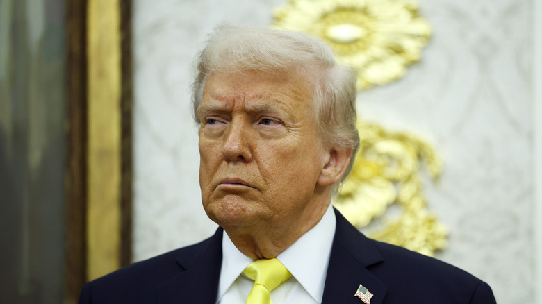 Donald Trump looking grumpy in a black suit with a yellow tie