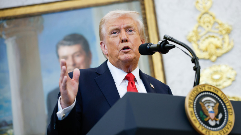 Donald Trump speaking at a podium in a black suit with a red tie