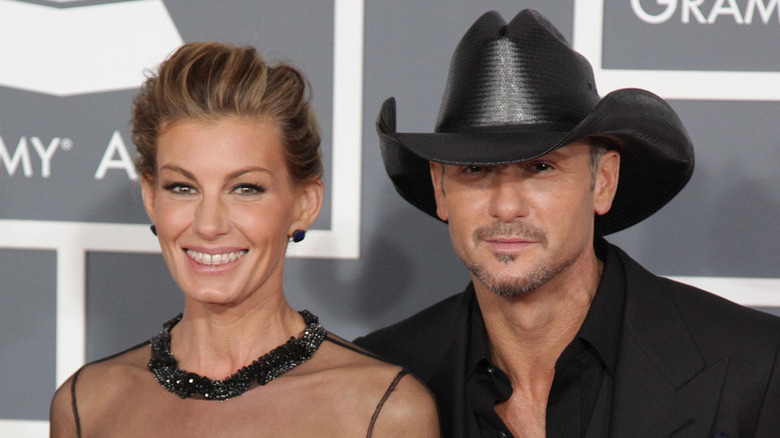 Faith Hill wearing a sheer black gown and Tim McGraw wearing a black jacket and collared shirt with a black cowboy hat