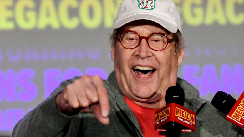 Chevy Chase pointing while holding a microphone