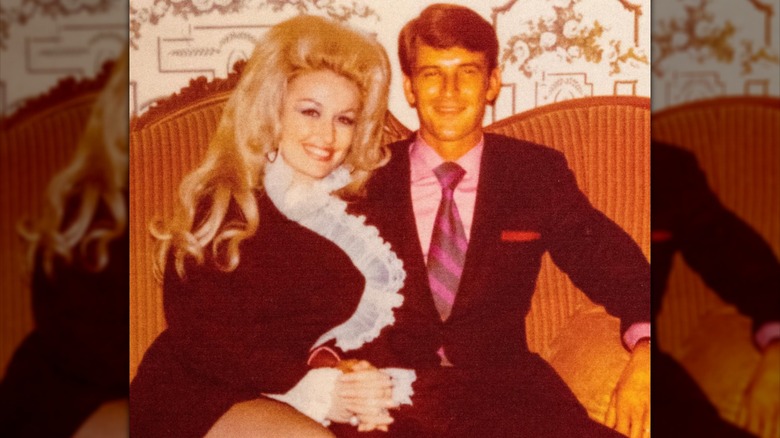 Dolly Parton and Carl Dean smiling while posing on a couch together