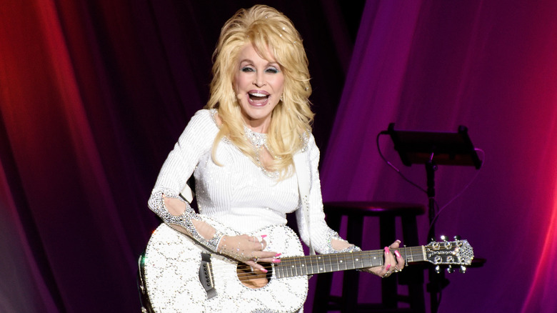 Dolly Parton laughing while performing on stage in a sparkly white outfit in 2016