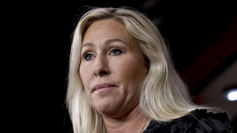 Marjorie Taylor Greene peaks at a press conference in 2023