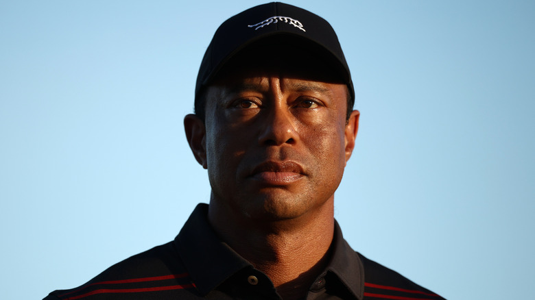 Close-up of Tiger Woods wearing a black hat and black and red striped polo shirt.
