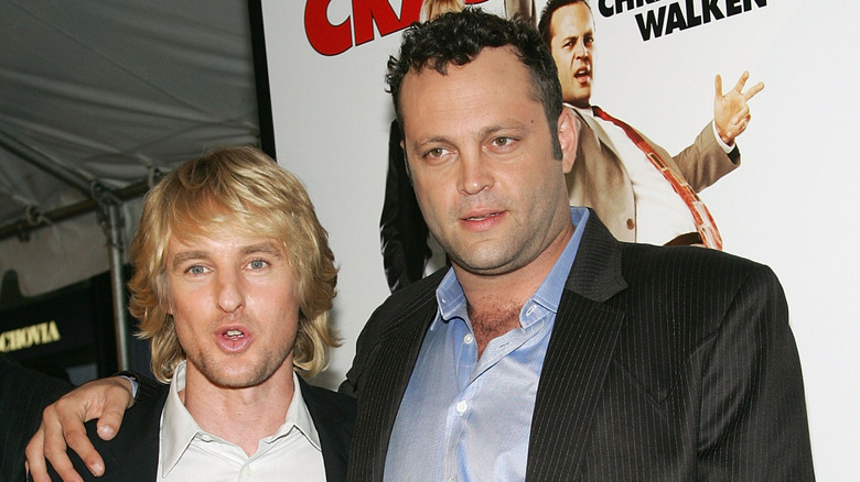 Owen Wilson and Vince Vaughn in front of a poster for Wedding Crashers