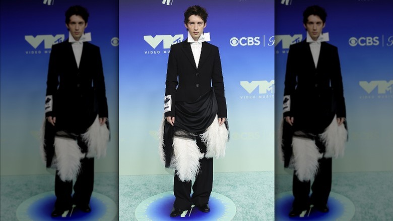 Troye Sivan wearing a suit with feathers and draped fabric at the waist