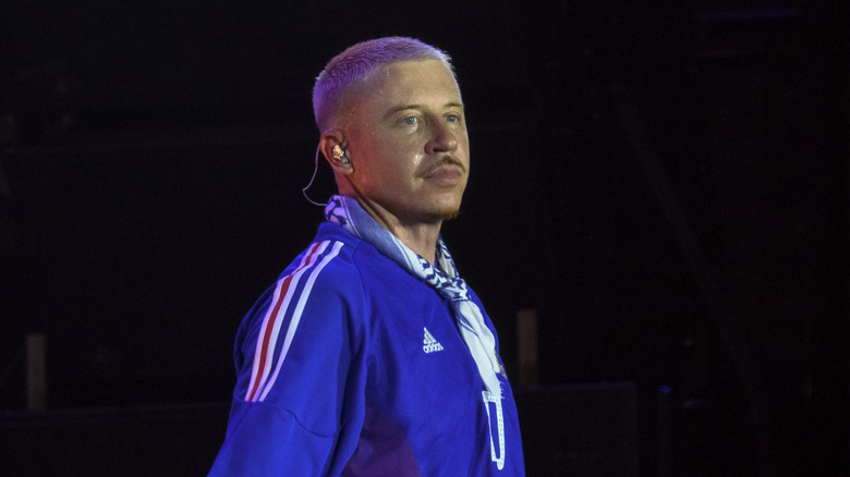 Macklemore wearing a blue Adidas jacket during a concert