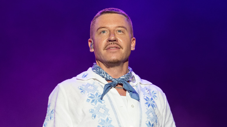 Macklemore in concert, standing in front of a purple background