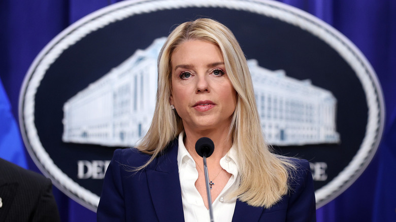 Pam Bondi speaking at a podium in a navy blazer with a white blouse underneath