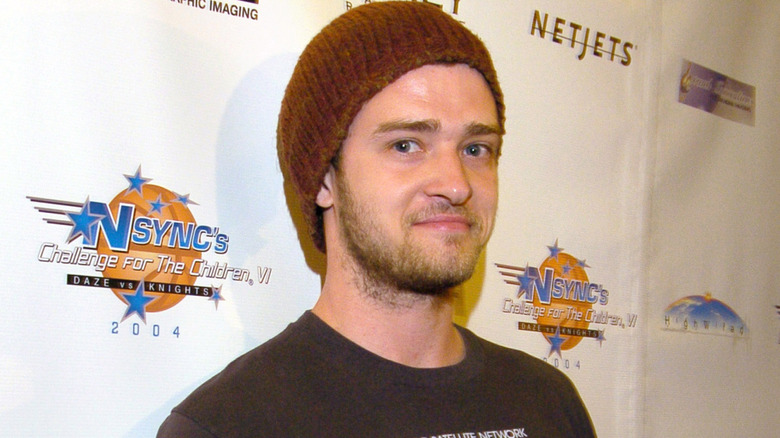 Justin Timberlake smirking at the camera while wearing a brown beanie and brown t-shirt