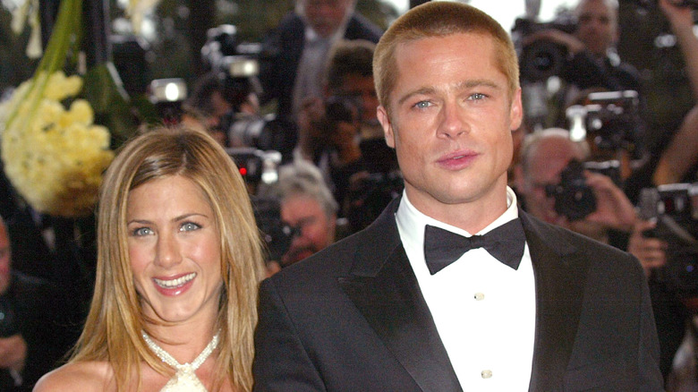 Jennifer Aniston wearing a white dress smiling next to Brad Pitt wearing a tuxedo