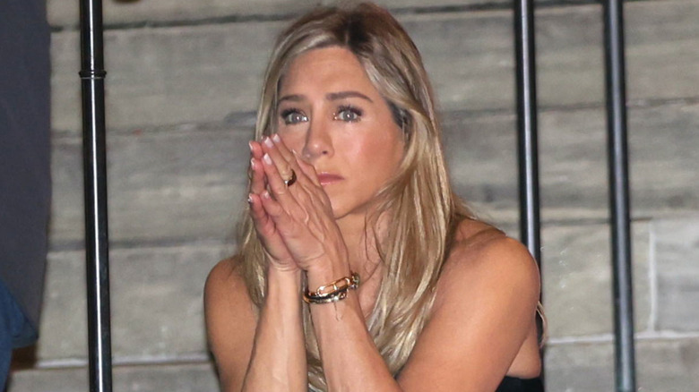 Jennifer Aniston sitting on stairs teary eyed with her hands in front of her face
