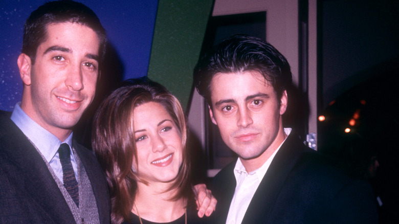 David Schwimmer wearing a suit and tie with Jennifer Aniston with a short haircut and Matt LeBlanc wearing a black jacket and white shirt