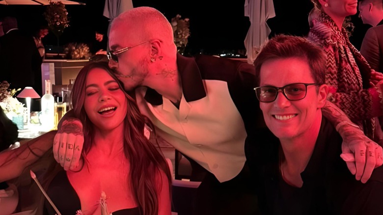 Sofía Vergara being kissed by a friend as she sits with Tom Brady