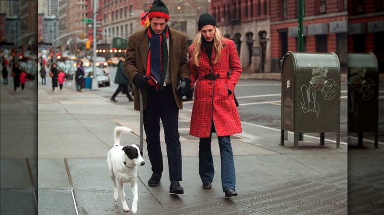Carolyn Bessette-Kennedy and John F. Kennedy Jr. wearing winter wear while walking their dog on an NYC sidewalk.