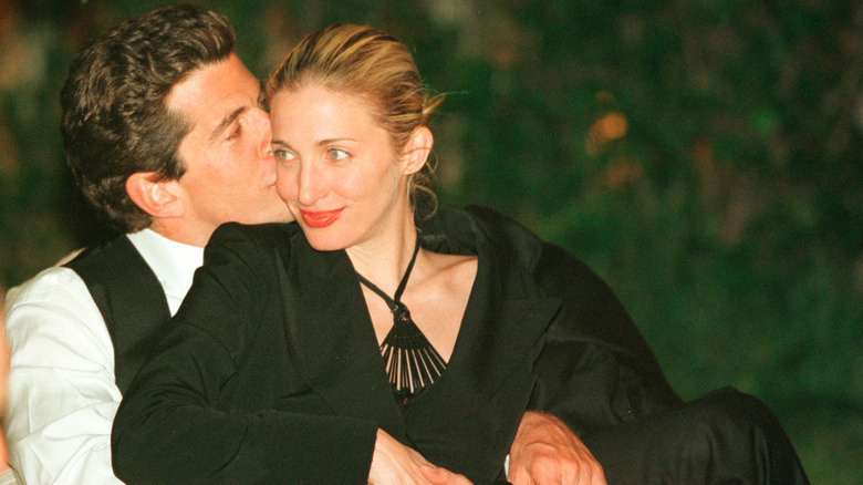 John F. Kennedy Jr. kisses Carolyn Bessette-Kennedy on the cheek as she smiles.