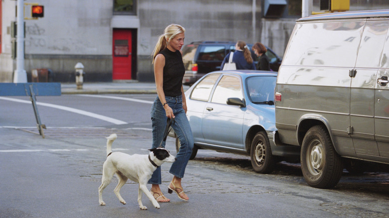 Carolyn Bessette-Kennedy wearing a black sleeveless top and jeans and walking her dog.