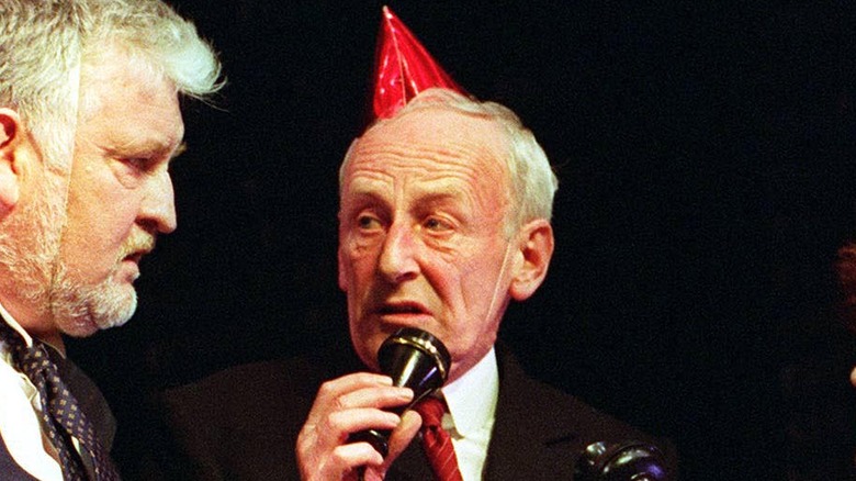 James Greene acting on stage with a party hat on his head, holding up a telephone to his mouth