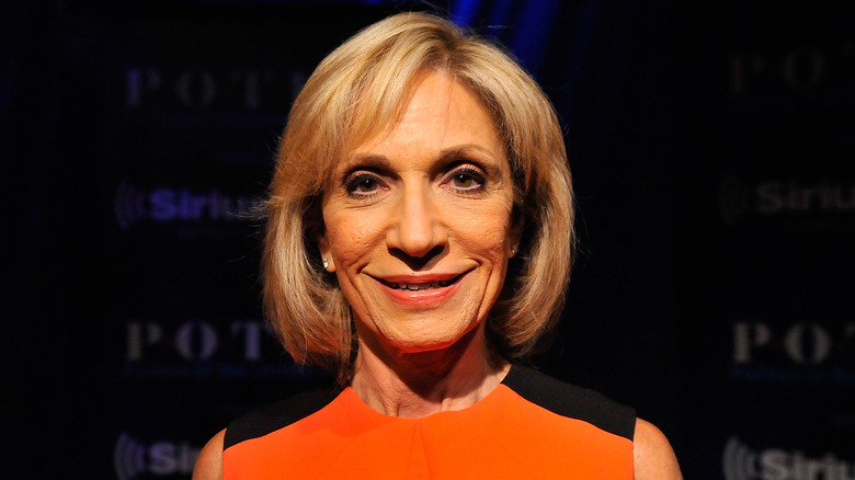 Andrea Mitchell smiling in an orange and black dress
