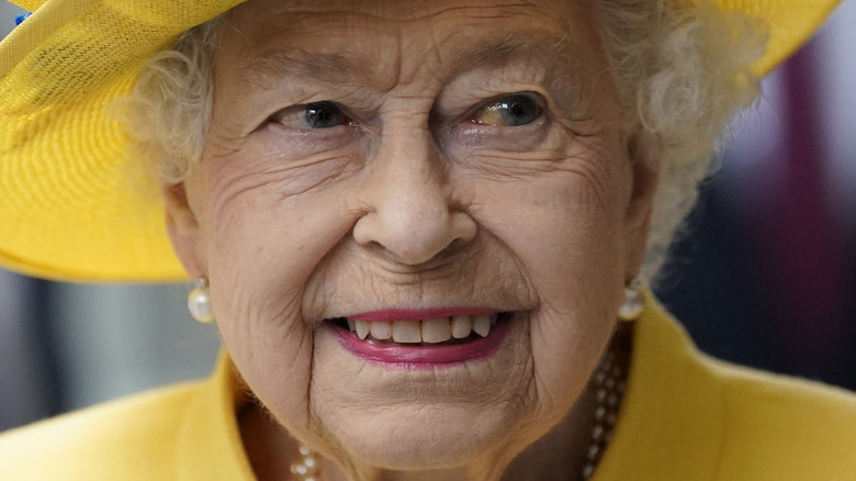 Queen Elizabeth II, wearing a yellow hat and coat with pearl earrings