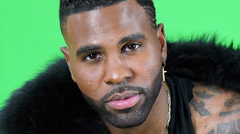 Jason Derulo, not smiling, smoldering, short hair, facial hair, fur collar, green background