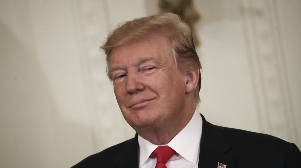 Donald Trump smirks at the camera while wearing a black suit