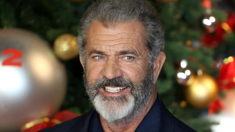 Mel Gibson grinning by a Christmas tree