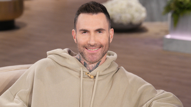 Adam Levine smiling and sitting in a chair