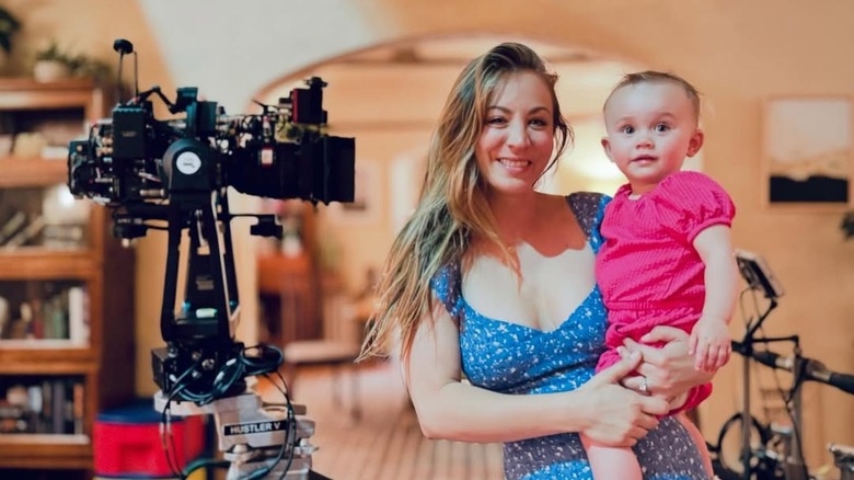 Kaley Cuoco wearing a blue flowered sundress holding her baby daughter Matilda wearing a pink onesie