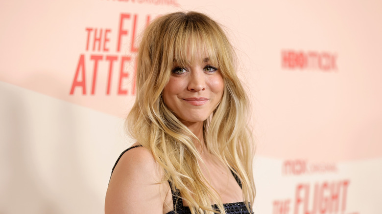 Kaley Cuoco with long blonde hair and bangs wearing a black strappy gown