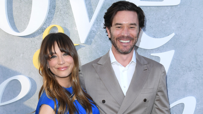 Kaley Cuoco with long brown hair and bangs wearing a blue high collared dress with Tom Pelphrey wearing a gray suit jacket and white collared shirt