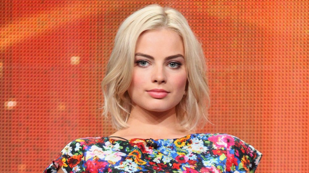 Margot Robbie in a floral dress, with a neutral expression, during a panel interview