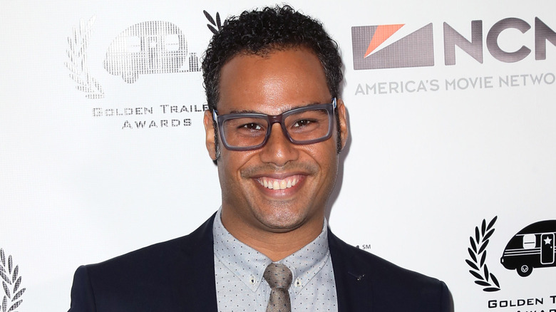Joshua Silverstein smiles while wearing glasses, dark blue blazer, and polka-dot shirt and tie