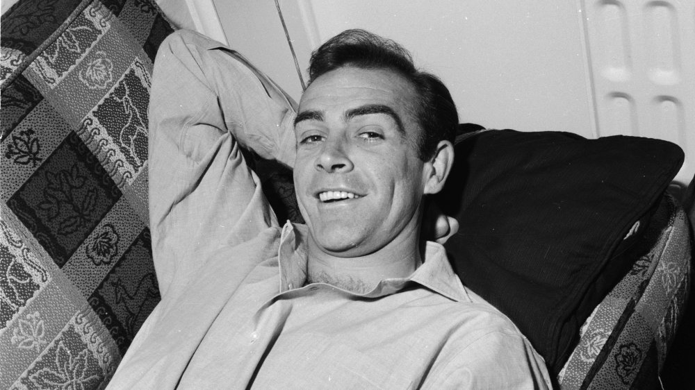 A young Sean Connery smiling while laying down on a couch