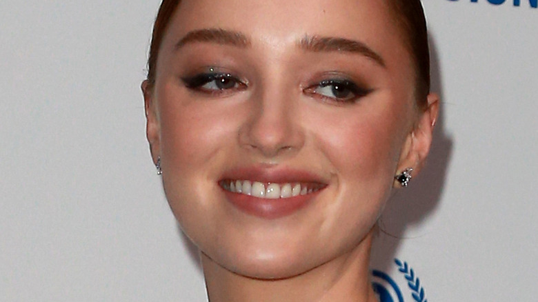 Phoebe Dynevor smiling and looking to the side on a red carpet 