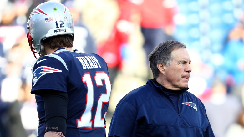 Tom Brady and Bill Belichick stand back to back on football field