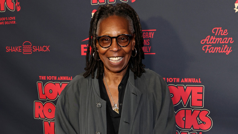 Whoopi Goldberg wearing a gray jacket and laughing at an event