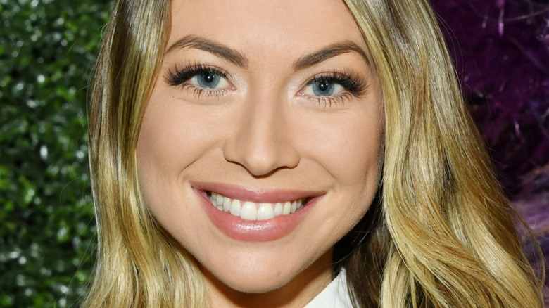 Closeup of Stassi Schroeder smiling, green and purple background
