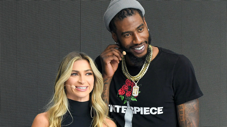 Iman Shumpert and Daniella Karagach smiling and speaking into headset microphones.
